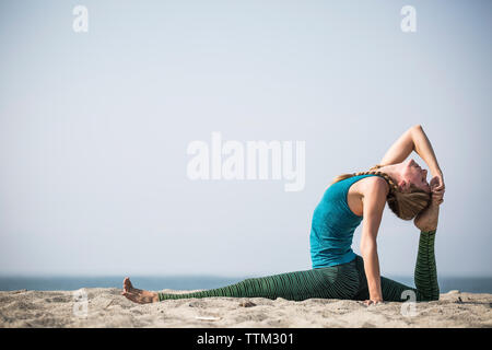 Vue latérale du woman exercising on sand at beach contre ciel clair Banque D'Images