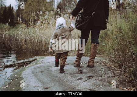 La section basse de mother holding daughter part en marchant par le lac en forêt Banque D'Images