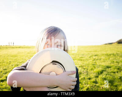 Portrait of boy holding hat while standing on grassy field against sky Banque D'Images
