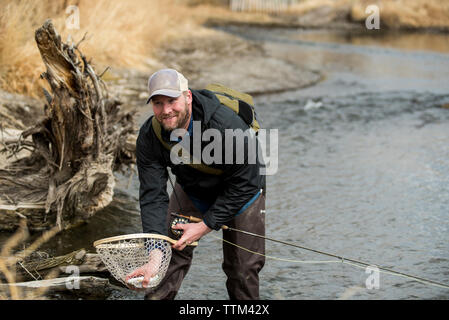 Smiling man l'enlèvement du poisson du filet de pêche papillon en position debout dans la rivière Banque D'Images