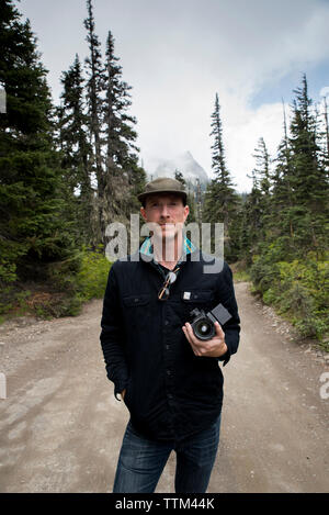 Portrait de l'homme tenir l'appareil photo en se tenant sur le route contre ciel nuageux dans le parc national Olympic Banque D'Images