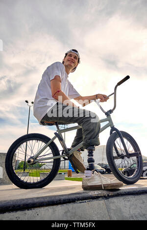 Rider BMX pied prothétique avec pose en toute confiance sur le vélo contre ciel nuageux au parc de planche à roulettes Banque D'Images