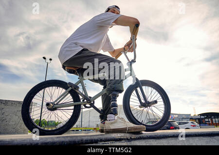 Rider BMX pied prothétique avec pose en toute confiance sur le vélo contre ciel nuageux au parc de planche à roulettes Banque D'Images