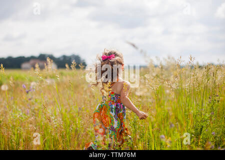 Vue arrière de fille avec l'exécution on grassy field against sky Banque D'Images