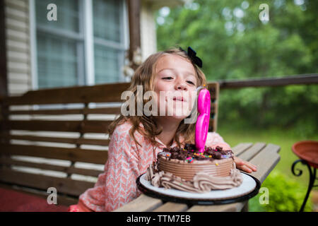 Girl blowing out numéro 6 bougie sur le gâteau d'anniversaire au porche Banque D'Images