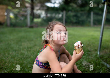 Portrait of Girl holding ice cream cone while sitting in yard Banque D'Images