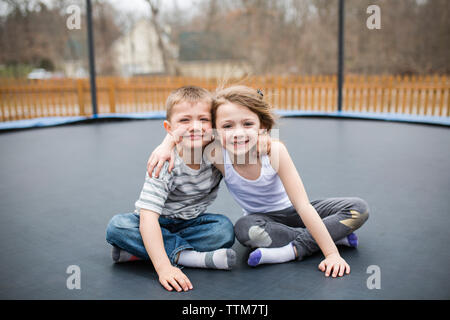 Portrait of happy siblings sitting on trampoline aire de jeux Banque D'Images