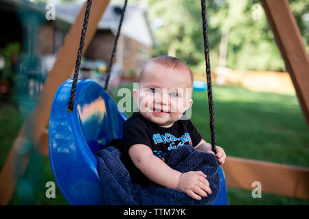 Portrait of cute baby boy sitting in swing à l'arrière-cour Banque D'Images