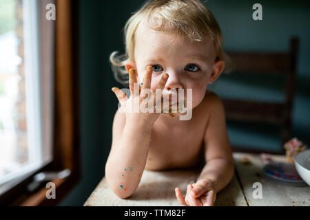 Bébé fille léchant les doigts collants avec sprinkles colorés Banque D'Images