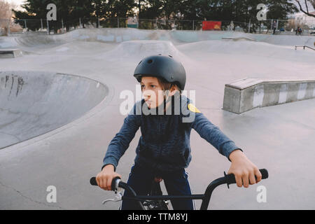 Boy wearing helmet, assis sur vélo au parc de planche à roulettes Banque D'Images