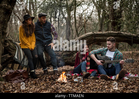 L'homme qui joue de la guitare alors qu'il était assis avec des amis dans la forêt d'Epping Banque D'Images