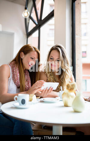 Happy female friends using mobile phone at cafe table Banque D'Images