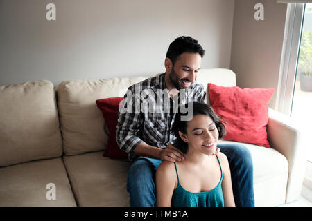 Smiling copain copine massage cou alors sitting on sofa at home Banque D'Images