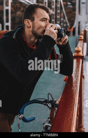 Bel appareil photo photographier avec cycliste en position debout avec location sur pont en ville pendant le coucher du soleil Banque D'Images