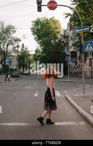 Femme rousse de cheveux tout en jetant crossing road in city Banque D'Images