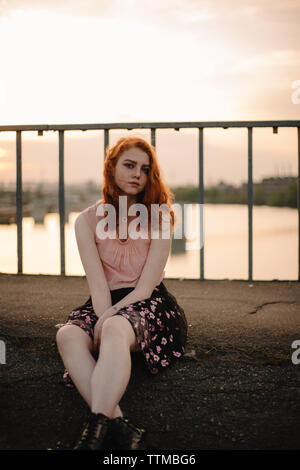 Jeune femme rousse assise sur bridge en ville Banque D'Images