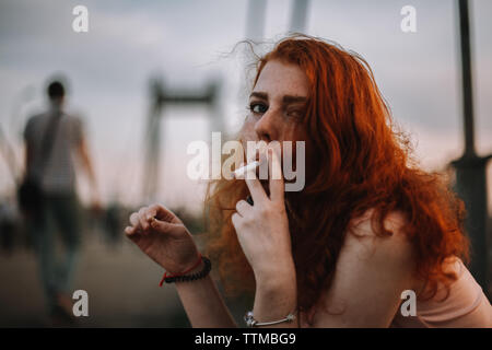 Jeune femme rousse de cigarette assis sur le pont en ville Banque D'Images