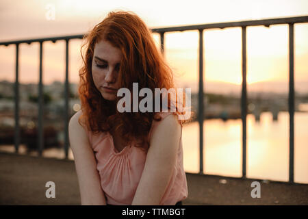 Portrait de jeune femme aux cheveux rouges assis sur le pont au coucher du soleil Banque D'Images