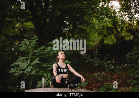 Woman meditating in lotus position au contre des arbres du parc Banque D'Images