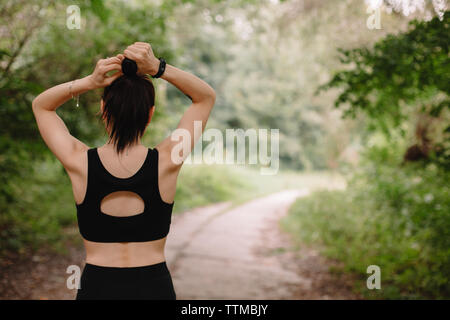 Vue arrière du female jogger faire hair bun at park Banque D'Images