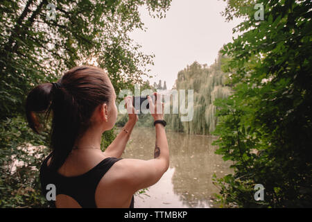 Rear view of woman photographing lake avec smart phone Banque D'Images