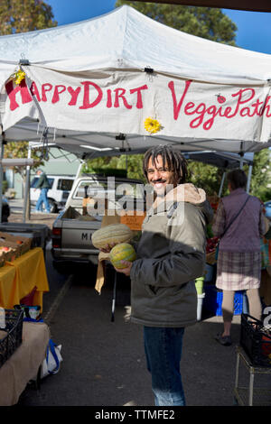 USA (Oregon), Ashland, producteurs et artisans de Rogue Valley Market, un homme achète des melons de l'heureuse saleté produire stand Banque D'Images