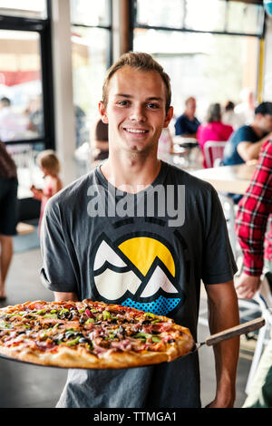 USA (Oregon, Bend, Pacific Pizza et Brew, man holding & presenting pizza Banque D'Images