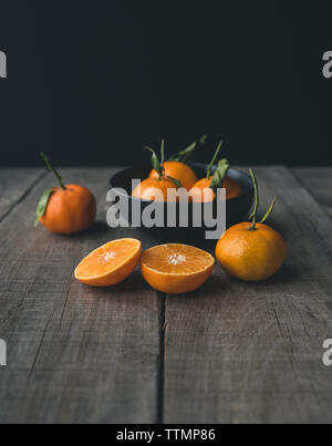 Des oranges dans le bol sur la table en bois sur fond noir Banque D'Images