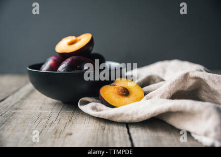 Close-up de prunes dans un bol avec serviette sur une table en bois à l'arrière-plan gris Banque D'Images