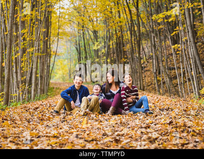 Mère ludique avec fils assis sur des feuilles sèches dans l'aménagement forestier Banque D'Images