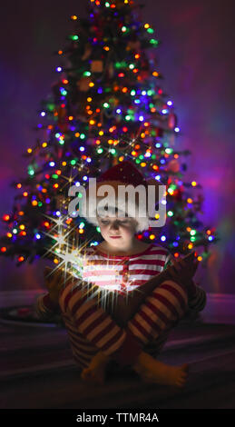 Jeune garçon lisant un livre magique en face de l'arbre de Noël. Banque D'Images