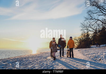 Père et fils de marcher un chien le long d'un chemin enneigé au coucher du soleil. Banque D'Images