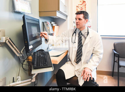 Un médecin en blouse blanche pointant sur l'écran d'ordinateur dans une salle de clinique. Banque D'Images
