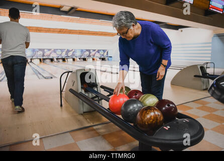 Femme plus âgée choisissant bowling ball comme homme à côté de son bol. Banque D'Images