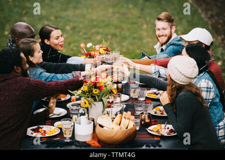 Happy friends toasting wine while sitting at table in backyard Banque D'Images