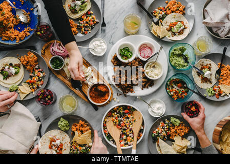 Mains coupées d'amis ayant la nourriture à table pendant le rassemblement social Banque D'Images