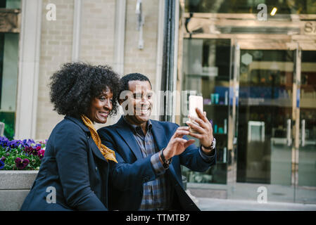 Couple heureux en tenant par selfies smart phone alors qu'il était assis sur le siège en ville Banque D'Images