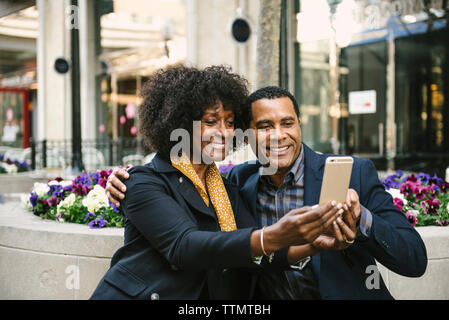 Smiling couple prenant en selfies smart phone alors qu'il était assis sur le siège en ville Banque D'Images