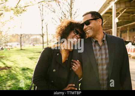 Heureux couple portant des lunettes de soleil tout en se tenant au parc Banque D'Images