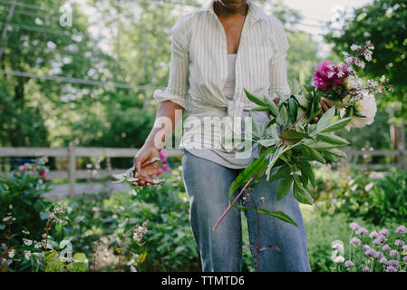 Portrait femme fleurs et d'un sécateur récoltés en étant debout dans le jardin Banque D'Images