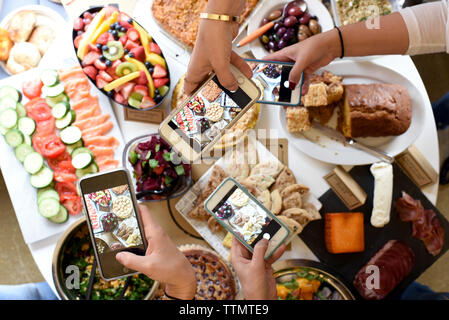 Les mains coupées des personnes photographiant les aliments par le biais de téléphones mobiles sur la table à buffet Banque D'Images