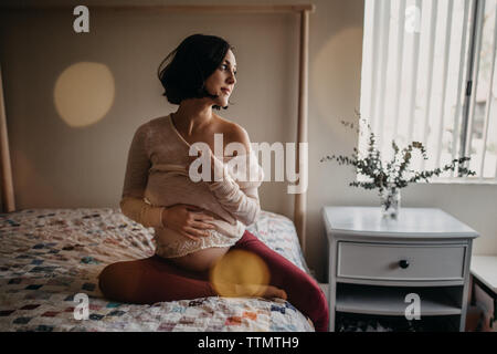 Pregnant woman holding baby bump au lit tout en souriant Banque D'Images