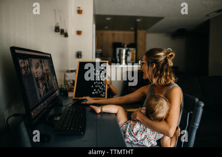 Mère au travail multitâche sur l'ordinateur et holding baby Banque D'Images