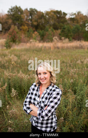 Portrait of smiling woman with arms crossed standing on grassy field in forest Banque D'Images