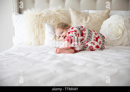 Sourire tout-petit Boy Wearing pyjamas de jette sur lit blanc Banque D'Images