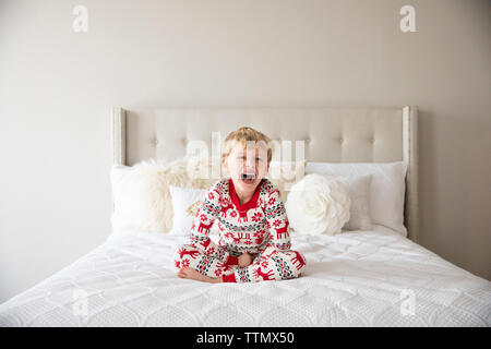 Cute Blonde Boy Wearing pyjamas de rire tandis que Sitting on Bed Banque D'Images