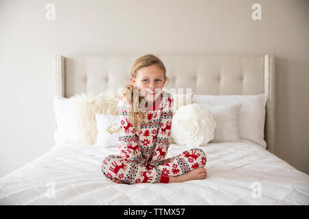 Jolie fille blonde aux cheveux bouclés dans la maison de vacances se trouve sur un lit blanc Pyjama Banque D'Images