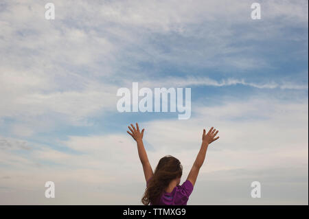 Vue arrière du Girl standing with arms raised against cloudy sky Banque D'Images