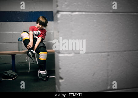 Boy putting sur patins de hockey sur glace Banque D'Images