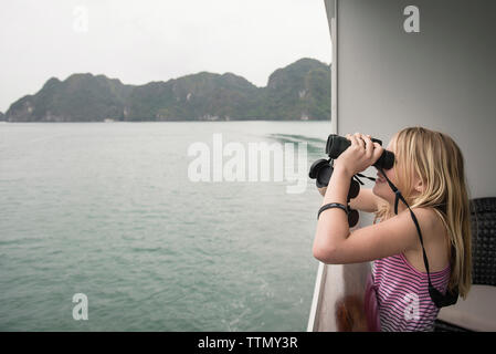 Vue latérale du girl looking through binoculars debout en bateau sur mer contre sky Banque D'Images